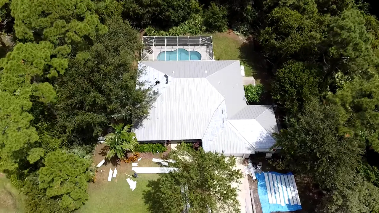 Aerial view of a completed white metal roof on a home with a backyard pool.
